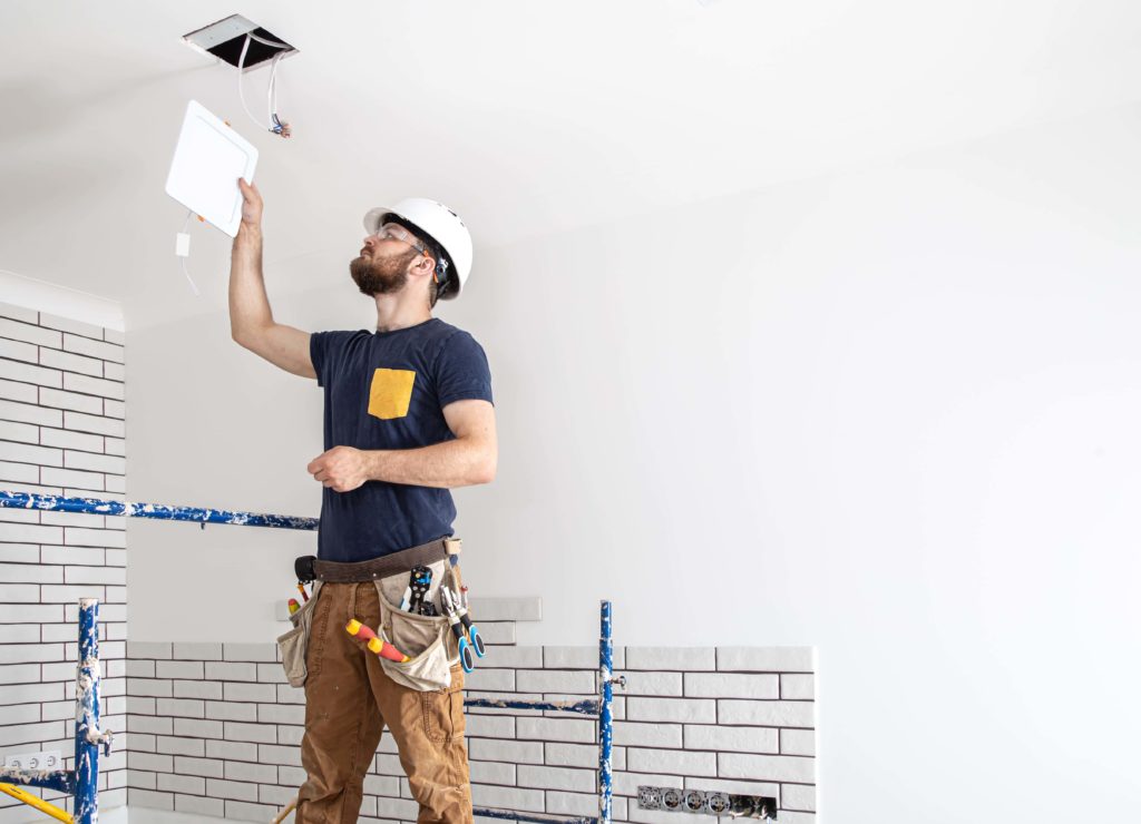 Smiling electrician fixing electric cable on ceiling